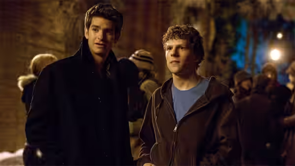 Jesse Eisenberg and Andrew Garfield stand together outdoors at night in a crowd
