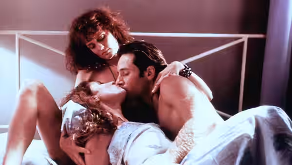 Randy kisses Sharon as another woman leans over them in bed