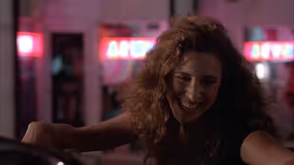 Sharon laughs at a nightclub, leaning across the bar
