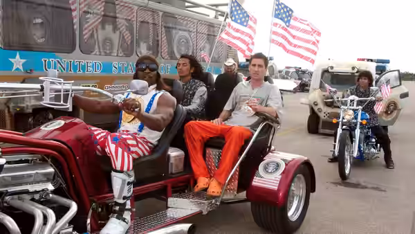 President Camacho (Terry Crews) riding in a red vehicle adorned with American flags