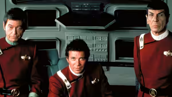 Kirk (William Shatner) seated between Spock (Leonard Nimoy) and another officer