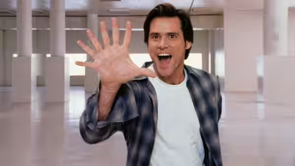 Bruce Nolan (Jim Carrey) extending an open hand forward with mouth agape indoors