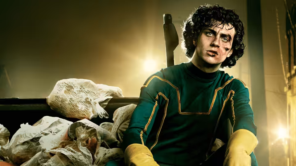 Kick-Ass (Aaron Taylor-Johnson) sitting bruised among garbage bags in green suit