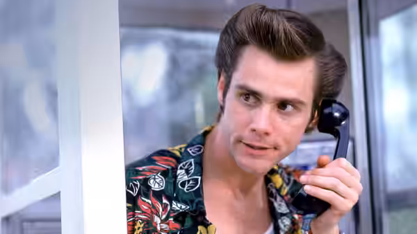 Ace Ventura (Jim Carrey) speaks on a telephone inside a phone booth