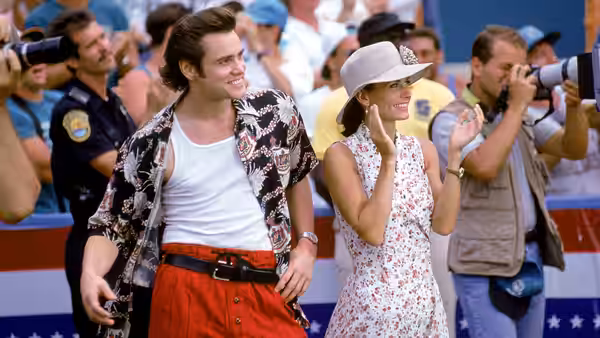 Ace Ventura (Jim Carrey) walks beside Melissa (Courteney Cox) past photographers