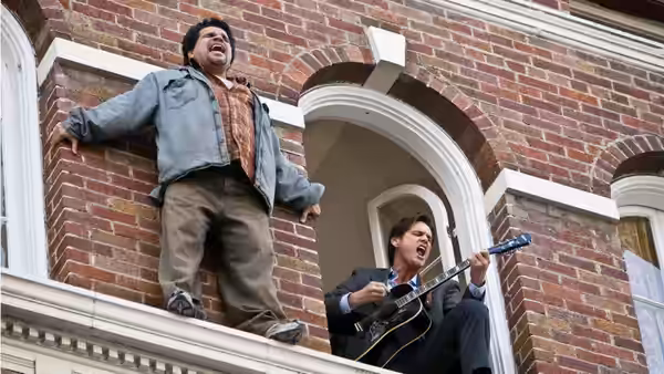 Two men sing from the ledge outside a brick building