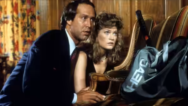 Fletch and Gail crouch beside an armchair, peering toward a sports bag