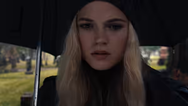 Sue Snell (Gabriella Wilde) gazes forward from under a black umbrella