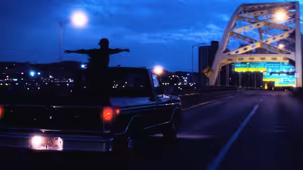 a person stands with arms outstretched on a truck crossing a bridge at night