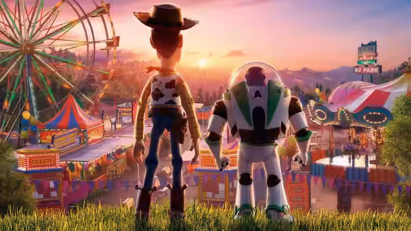 Woody and Buzz Lightyear standing in grass overlooking a carnival at sunset