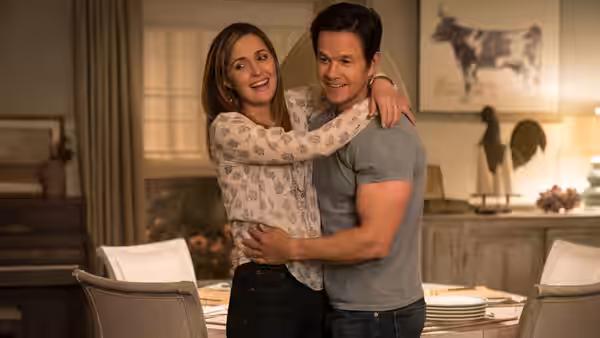 Ellie (Rose Byrne) hugging Pete (Mark Wahlberg) from behind in their dining room
