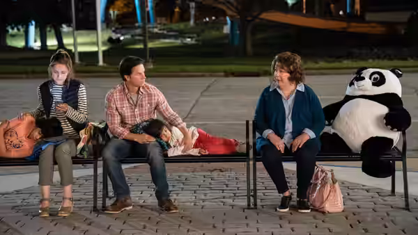 Pete (Mark Wahlberg) and Sandy (Margo Martindale) sitting with children and a giant panda on a bench