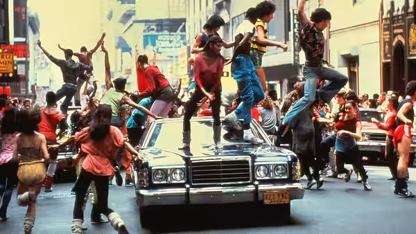 Students dance around a car in the middle of a city street