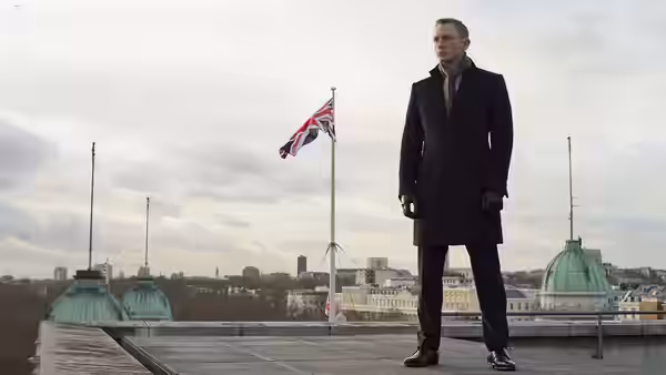 James Bond (Daniel Craig) in a dark overcoat on a rooftop with a Union Jack flag
