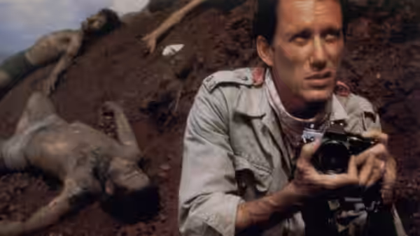 Richard Boyle (James Woods) clutches his camera beside bodies on a muddy hillside