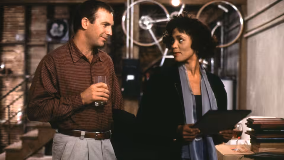 Frank Farmer (Kevin Costner) talks with Rachel Marron (Whitney Houston) in a room with recording equipment