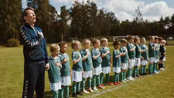 Peter (Lars Ranthe) sings with a line of young football players