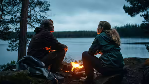 Martin and Anika sit beside a campfire by the lake