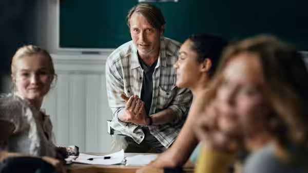Martin (Mads Mikkelsen) leans toward students in a classroom