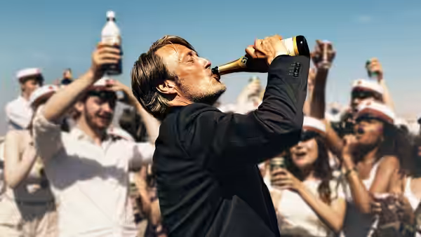 Martin (Mads Mikkelsen) drinks from a bottle as students celebrate around him
