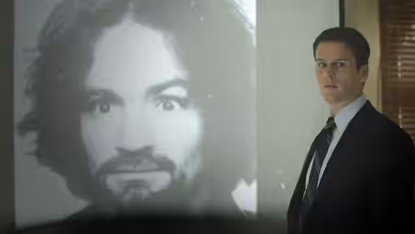 Holden Ford (Jonathan Groff) stands beside a projected portrait of a man