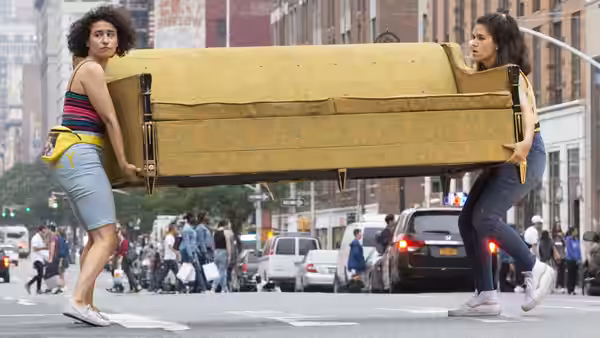 Abbi Abrams (Abbi Jacobson) and Ilana Wexler (Ilana Glazer) carrying a yellow couch across a city street