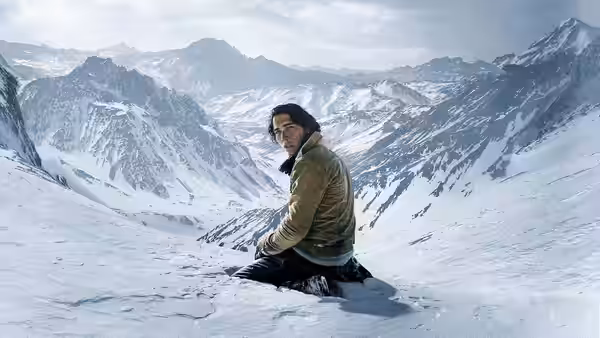 A lone man sits in the snow overlooking a vast range of mountains