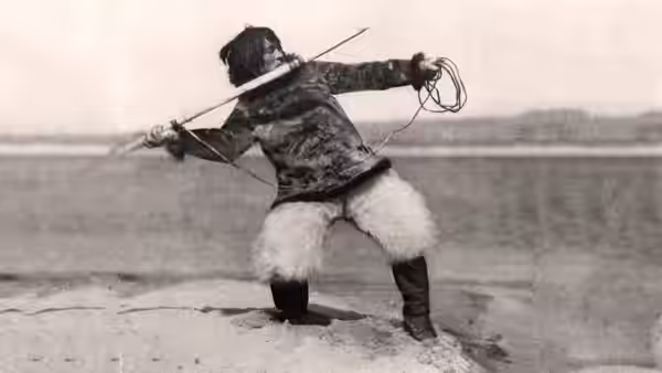 Nanook crouched on ice aiming a harpoon across the plain