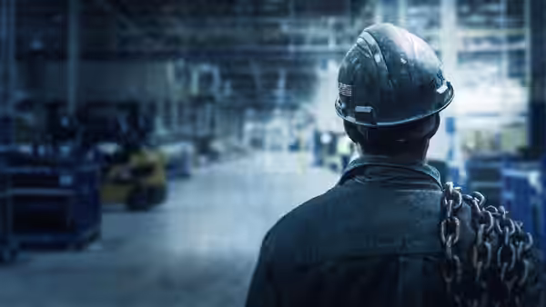 Worker in hard hat carrying chains walks through the empty plant