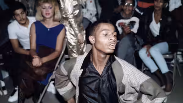 A young man performs with eyes closed amid an audience at an indoor event