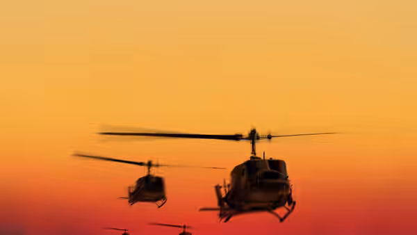 Helicopters fly in formation across an orange and red sunset sky