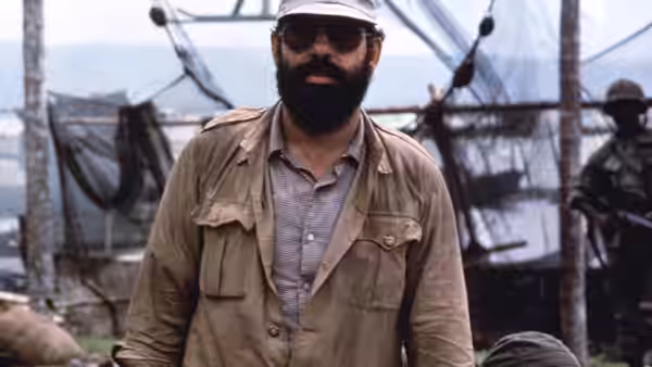 Francis Ford Coppola stands in military jacket sunglasses and cap on set