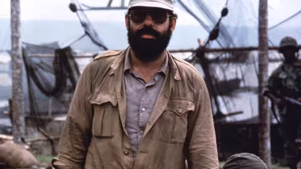 Francis Ford Coppola stands in military jacket sunglasses and cap on set