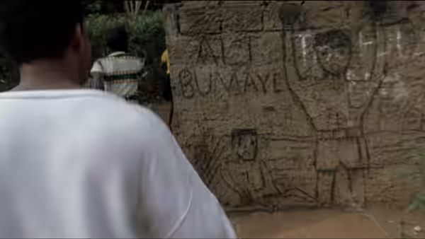A man in a white shirt looks at drawings and writing on a mud wall