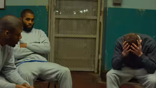 Three inmates sitting in a prison room one with head in hands