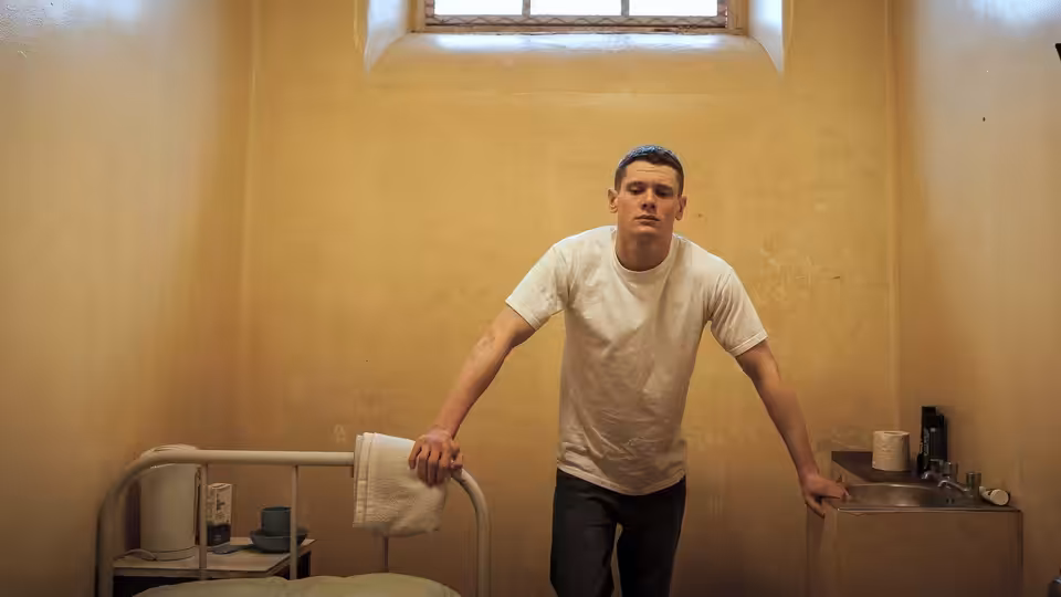 Eric Love (Jack O'Connell) standing in a sparse prison cell with hands on furniture