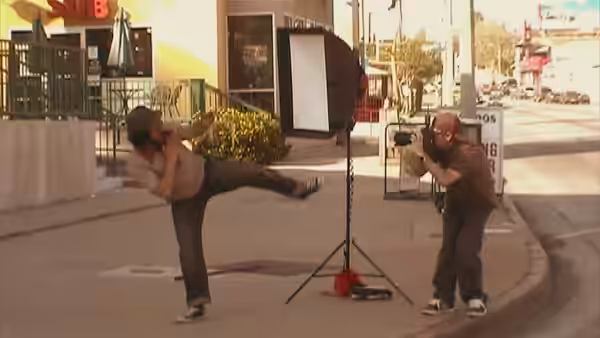 man films another kicking dynamically on a sunny urban sidewalk