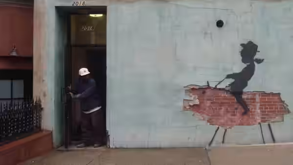 A hard-hatted worker enters a doorway beside a large stencil mural on the wall
