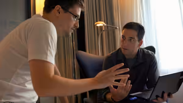 Edward Snowden gesturing to Glenn Greenwald who holds a laptop