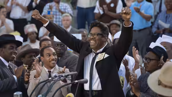 Bayard Rustin (Colman Domingo) raises his arms at a crowded rally as people applaud