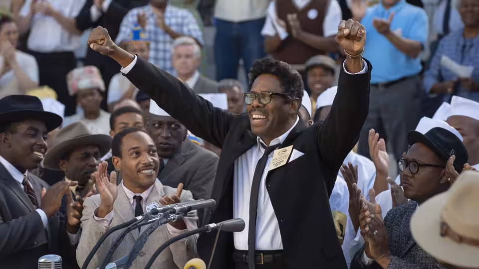 Bayard Rustin (Colman Domingo) raises his arms at a crowded rally as people applaud