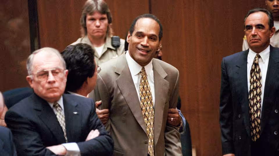 O. J. Simpson smiling while being escorted through a courtroom