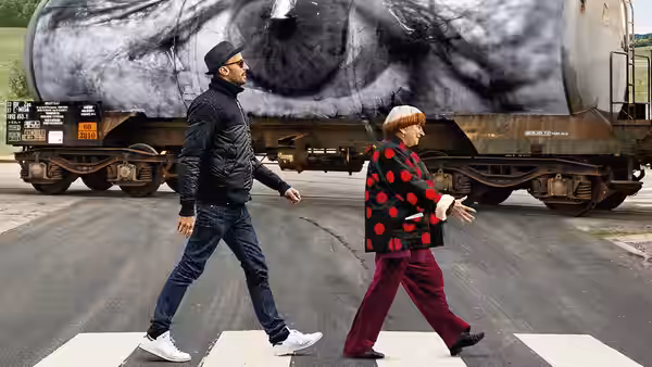 Agnès Varda (Agnès Varda) and JR cross a road by a train mural