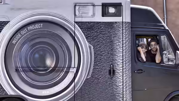 two people look out from a van beside a giant camera mural