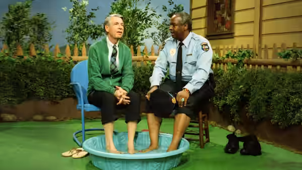Fred Rogers in green cardigan sits with a police officer in a basin
