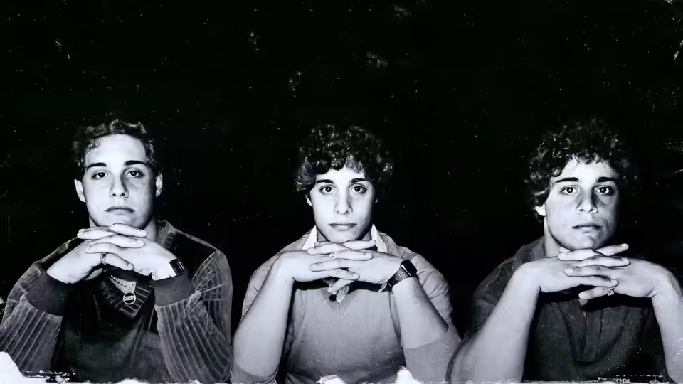Three young men with curly hair rest their chins on clasped hands