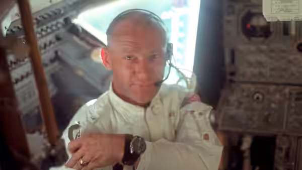 an astronaut seated in the spacecraft cockpit wearing a headset and smiling