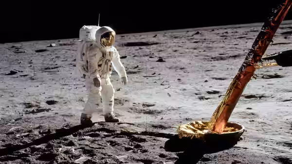 an astronaut stands on the lunar surface beside the module leg