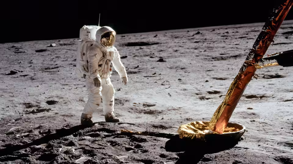 an astronaut stands on the lunar surface beside the module leg