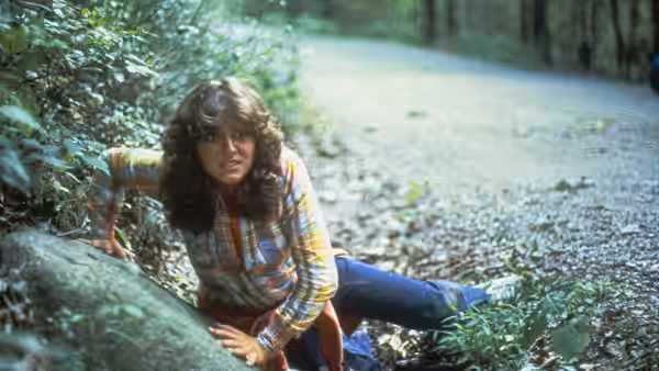 A young woman in a plaid shirt scrambles through the woods
